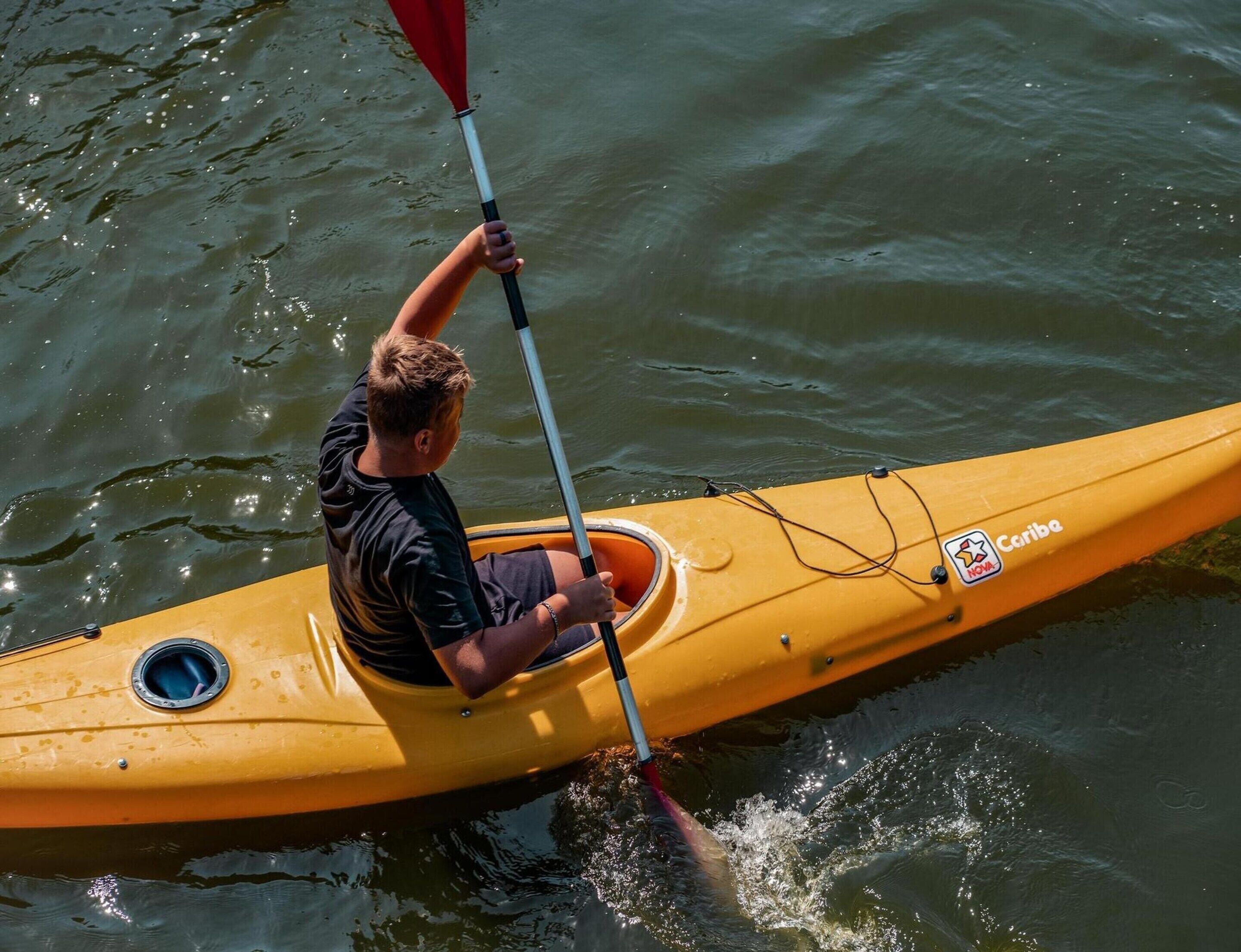 A person kayaking on a yellow kayak with a brand logo.