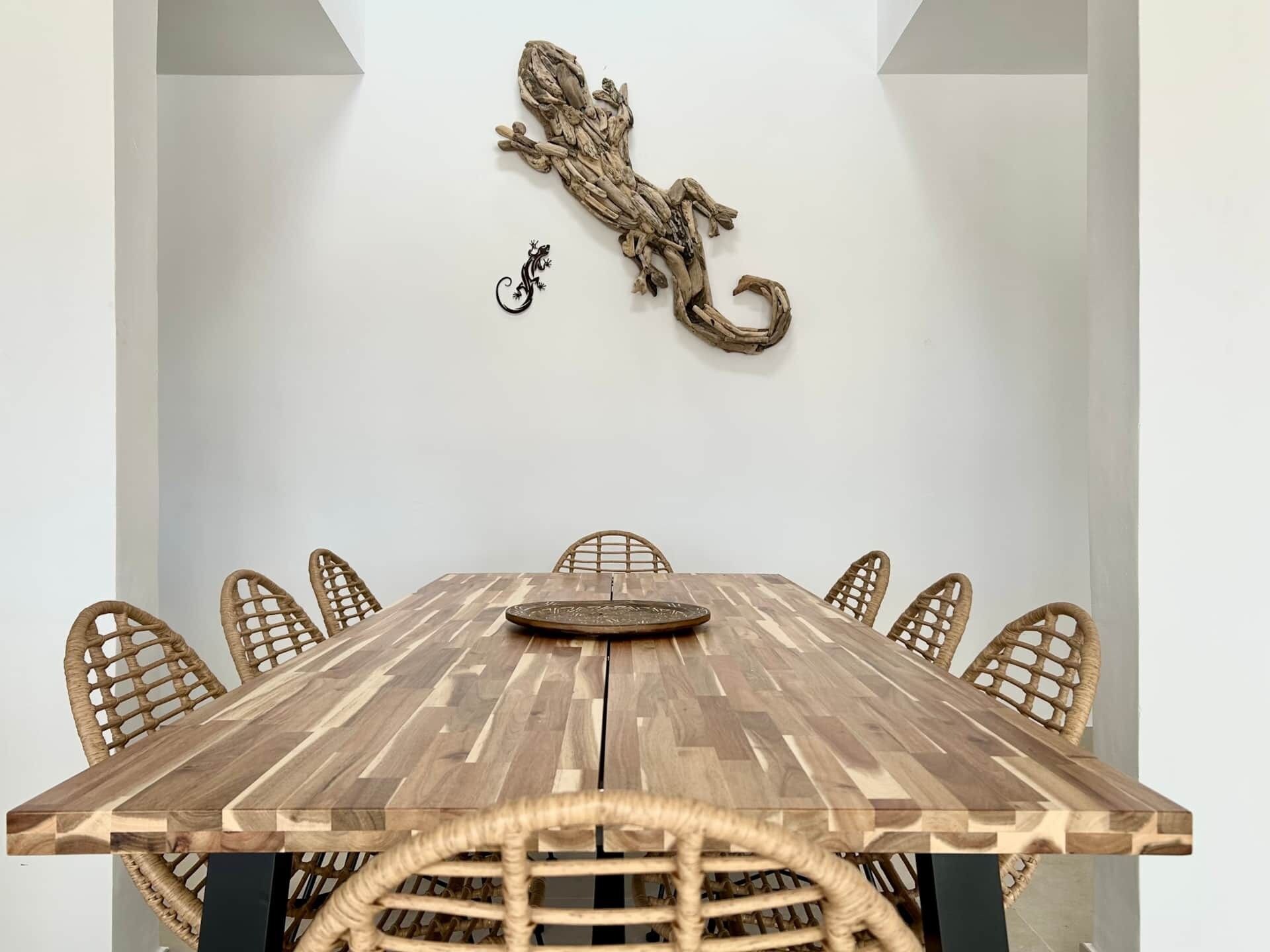 Ein Esstisch mit sechs Korbstühlen, einem Wanddekor und einer kleinen Skulptur.