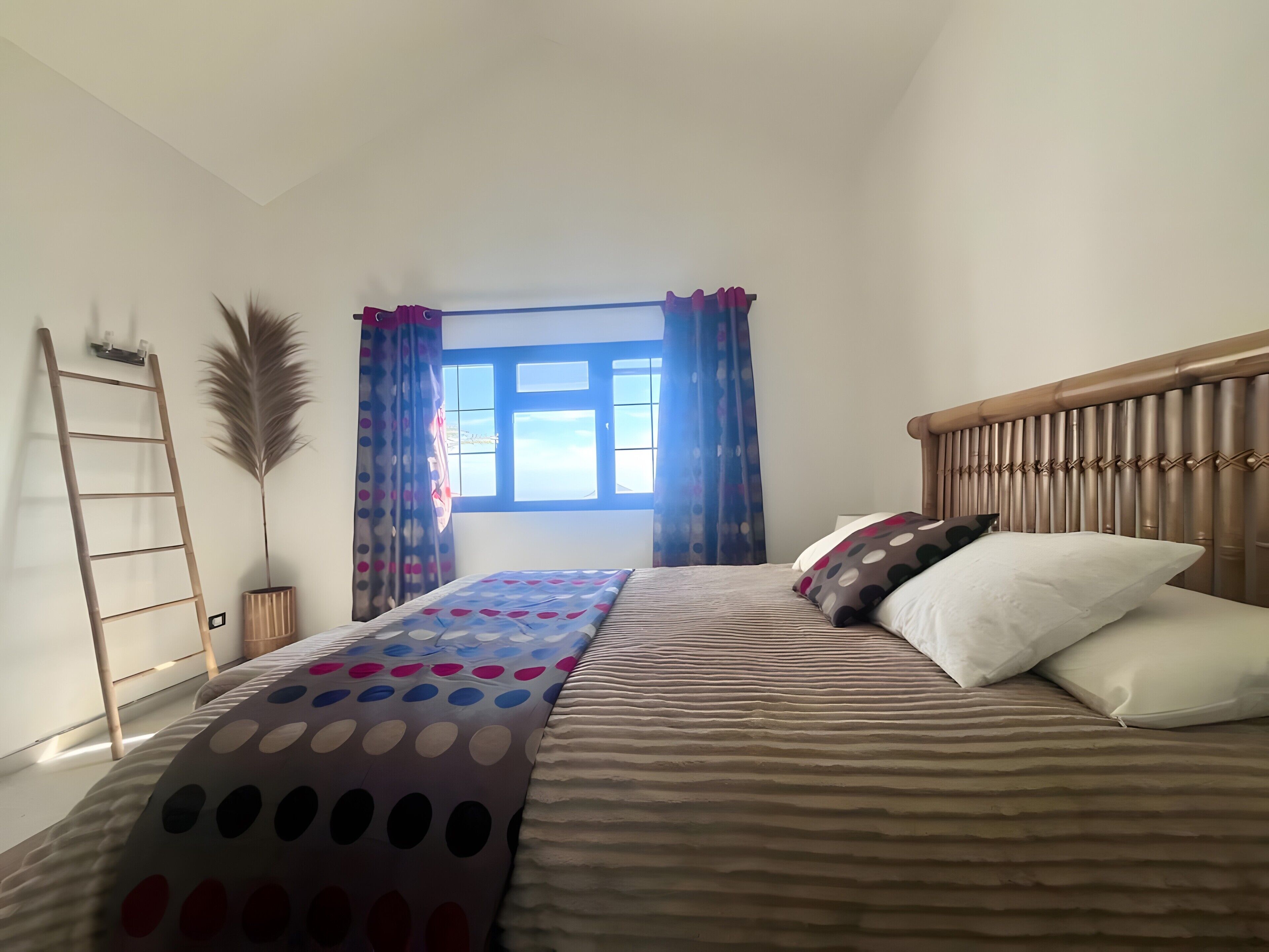 Une chambre à coucher avec un lit, une fenêtre avec des rideaux, une table de chevet et une étagère fixée au mur.