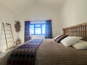 Een slaapkamer met een bed, een raam met gordijnen, een nachtkastje en een wandplank.