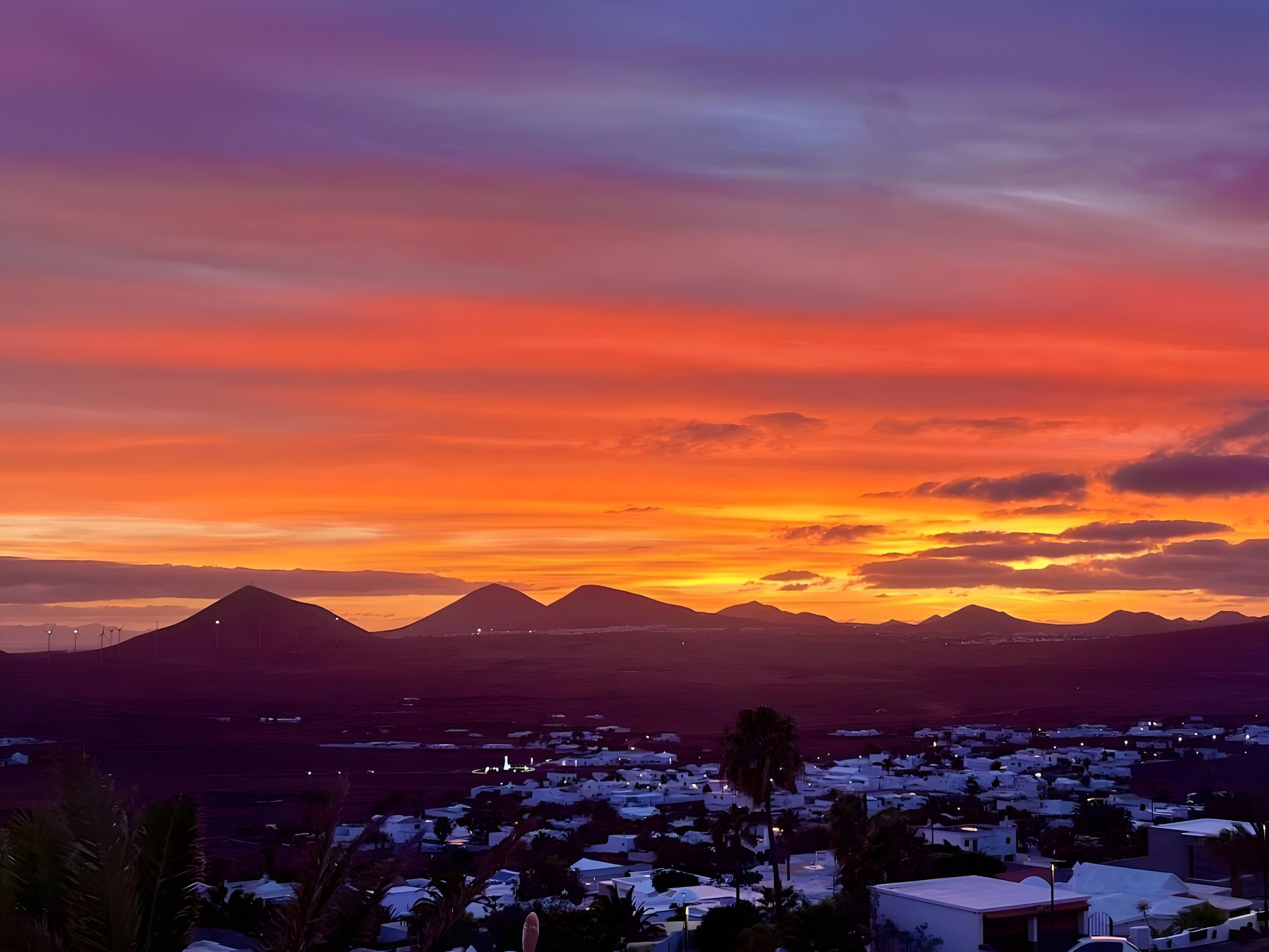 Une ville côtière au coucher du soleil, avec une chaîne de montagnes en arrière-plan.