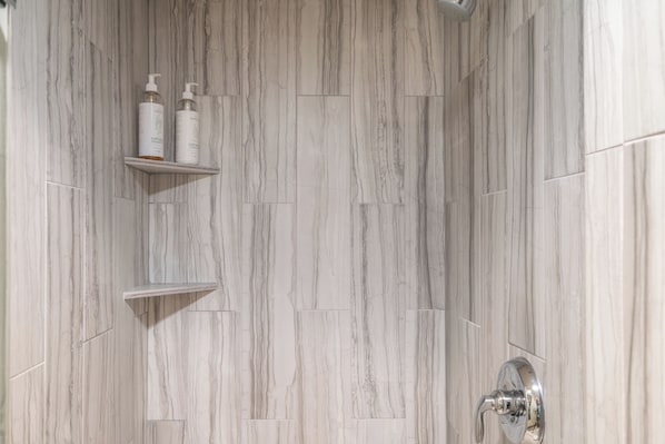 Een badkamer met een marmeren wand, een douchegedeelte en twee planken met toiletartikelen.