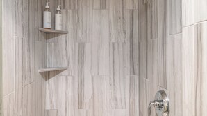 A bathroom with a marble wall, a shower area, and two shelves with toiletries. - Adjoining rooms create a wonderful space with modern finishes (Telluride)
