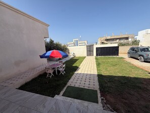 A residential backyard with a paved patio, a table with chairs, and a parked car.