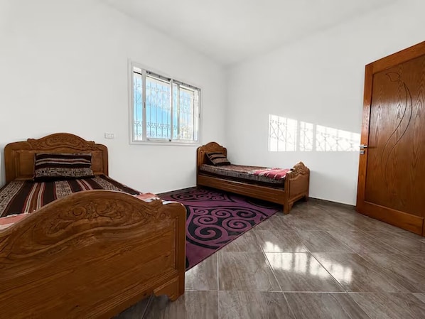 A room with two wooden beds, a window, and a door.