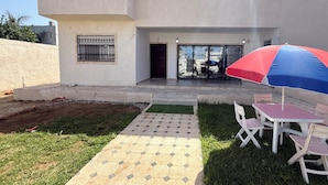 Ein modernes Haus mit gepflasterter Terrasse, kleinem Garten und einem Tisch mit Stühlen.