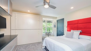 A bedroom with a bed, a red headboard, a ceiling fan, and a window with a view of greenery. - Kitchenette room with Queen bed and murphy bunk beds (Telluride)
