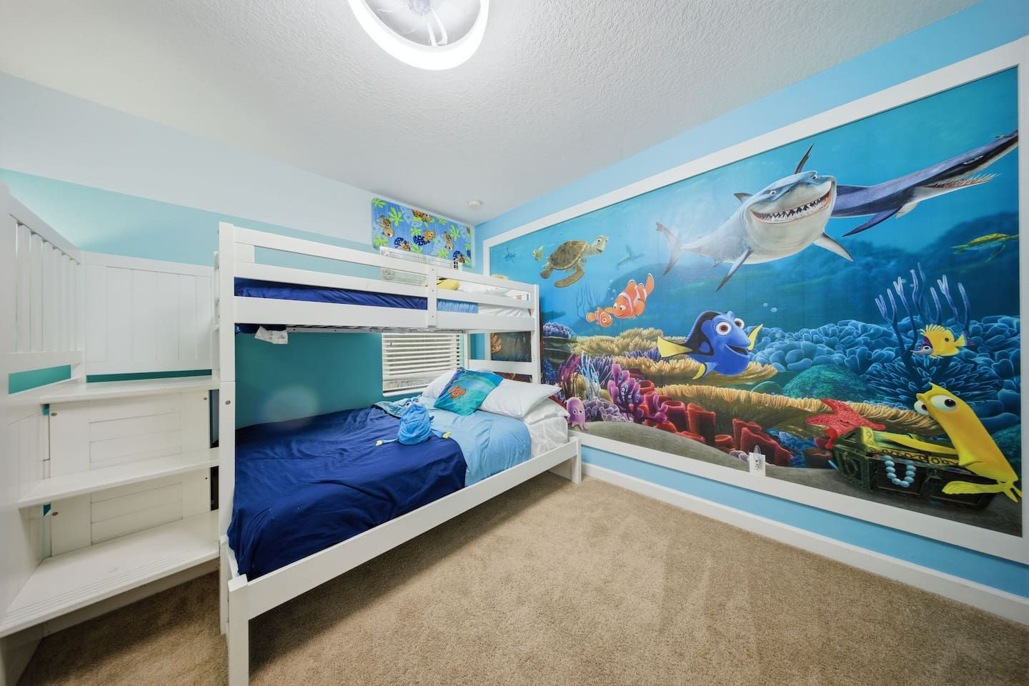 Un dormitorio infantil con literas, un mural de una escena submarina y una lámpara en el techo.