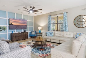 A living room with a sofa, armchair, coffee table, and a television mounted on the wall. - Lola’s Oasis | 5BR Pool Home + Lazy River + Disney (Four Corners)