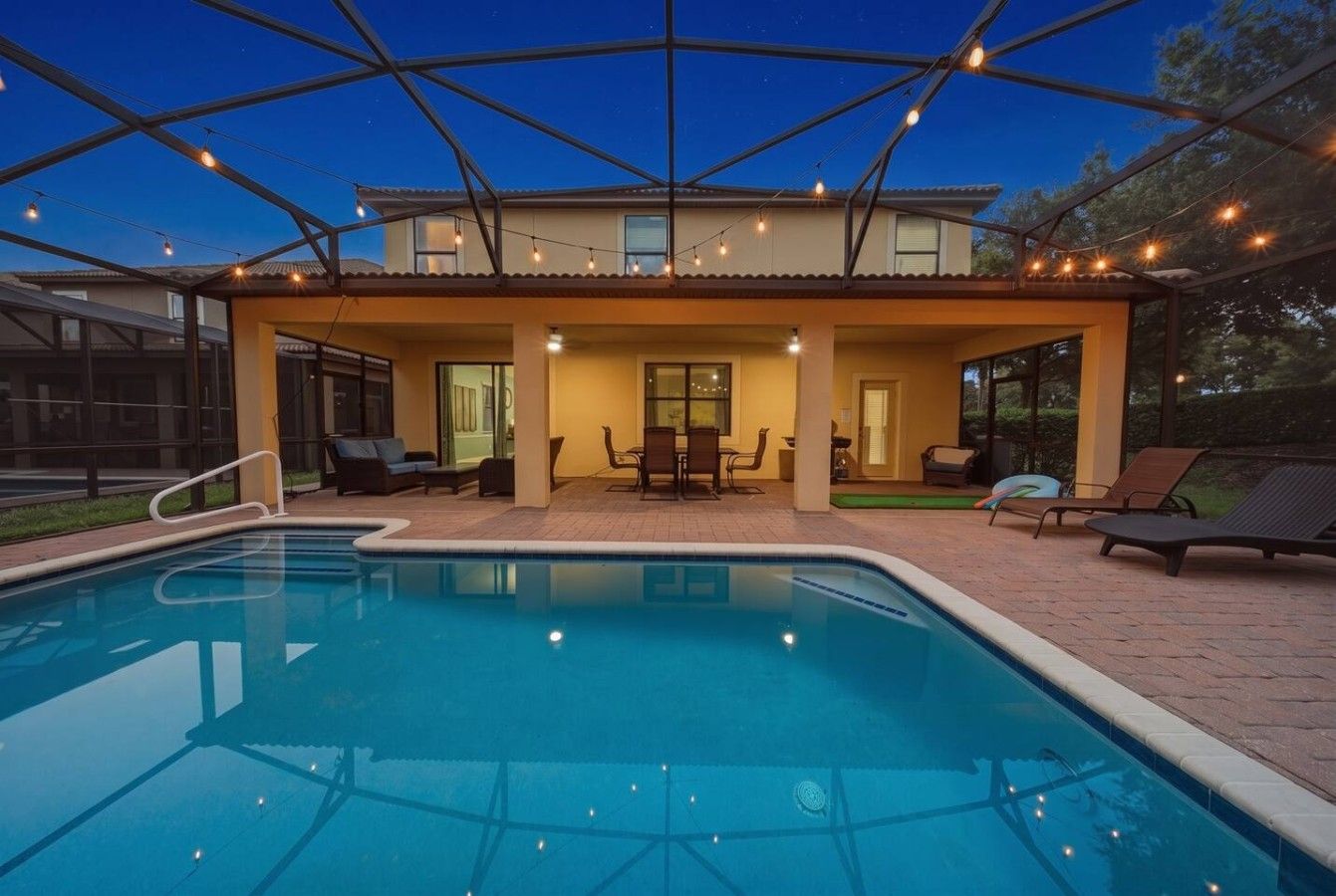 A swimming pool with a covered patio area, outdoor furniture, and string lights.