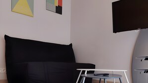 Moderni olohuone, jossa on musta sohva, pieni pöytä, jossa on kaukosäädin, ja seinälle asennettu taulutelevisio.