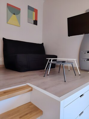 Ein zeitgemäßer Wohnraum mit einem schwarzen Sofa, einem kleinen Tisch mit Fernbedienung und einem wandmontierten Flachbildfernseher.