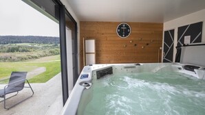 A hot tub with a wooden wall and a clock, a chair, and a view of the countryside. - Bed and Breakfast 'Chambre La Grande Ourse' with Lake View, Shared Terrace and Wi-Fi (Grande-Rivière Château)