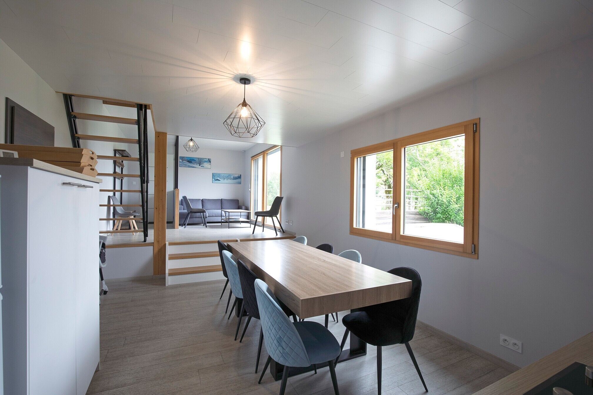 A modern kitchen with a dining area, wooden flooring, and a view through a window.