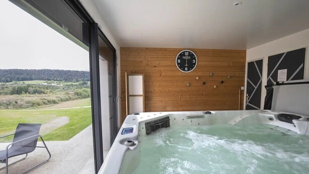 Un jacuzzi con pared de madera, un reloj, una silla y vistas al campo.