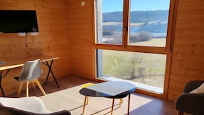 Habitación con paredes de madera, un ventanal grande, televisor de pantalla plana, una mesa de comedor y dos sillas.