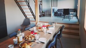Un comedor con una mesa de madera dispuesta para el desayuno, una escalera y un moderno espacio de sala con sofá y sillones.