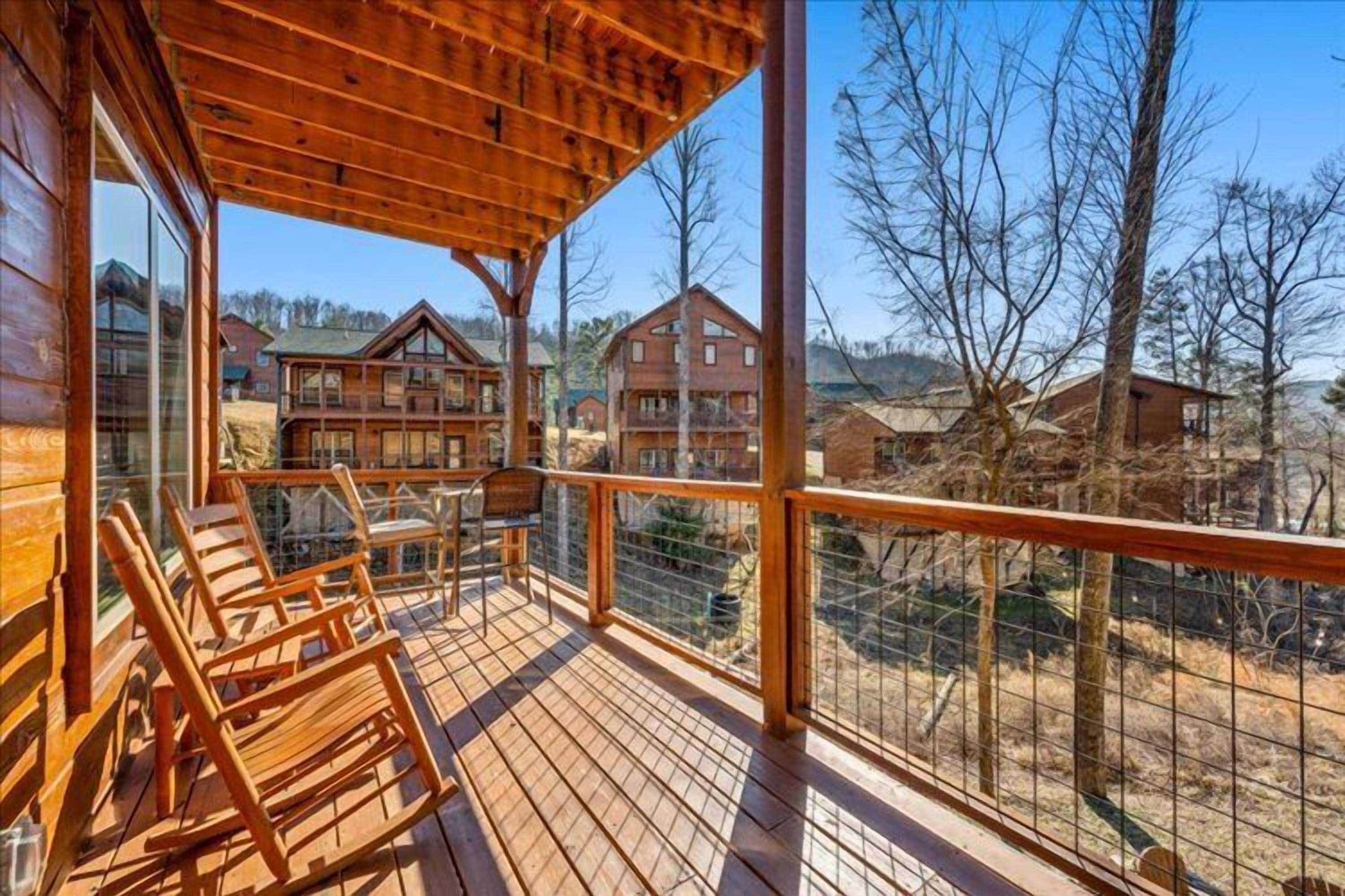 Eine Holzterrasse mit Stühlen und Tisch, mit Blick auf ein Wohngebiet mit Häusern und Bäumen.