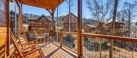 A wooden deck with chairs and a table, overlooking a residential area with houses and trees.