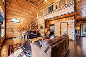 Ein geräumiges Holzhaus-Interieur mit Wohnbereich, einer Treppe und einem Balkon im zweiten Stock.