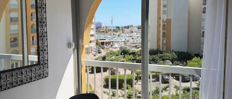 A balcony with a view of a cityscape, a dining table with chairs, and a potted plant.