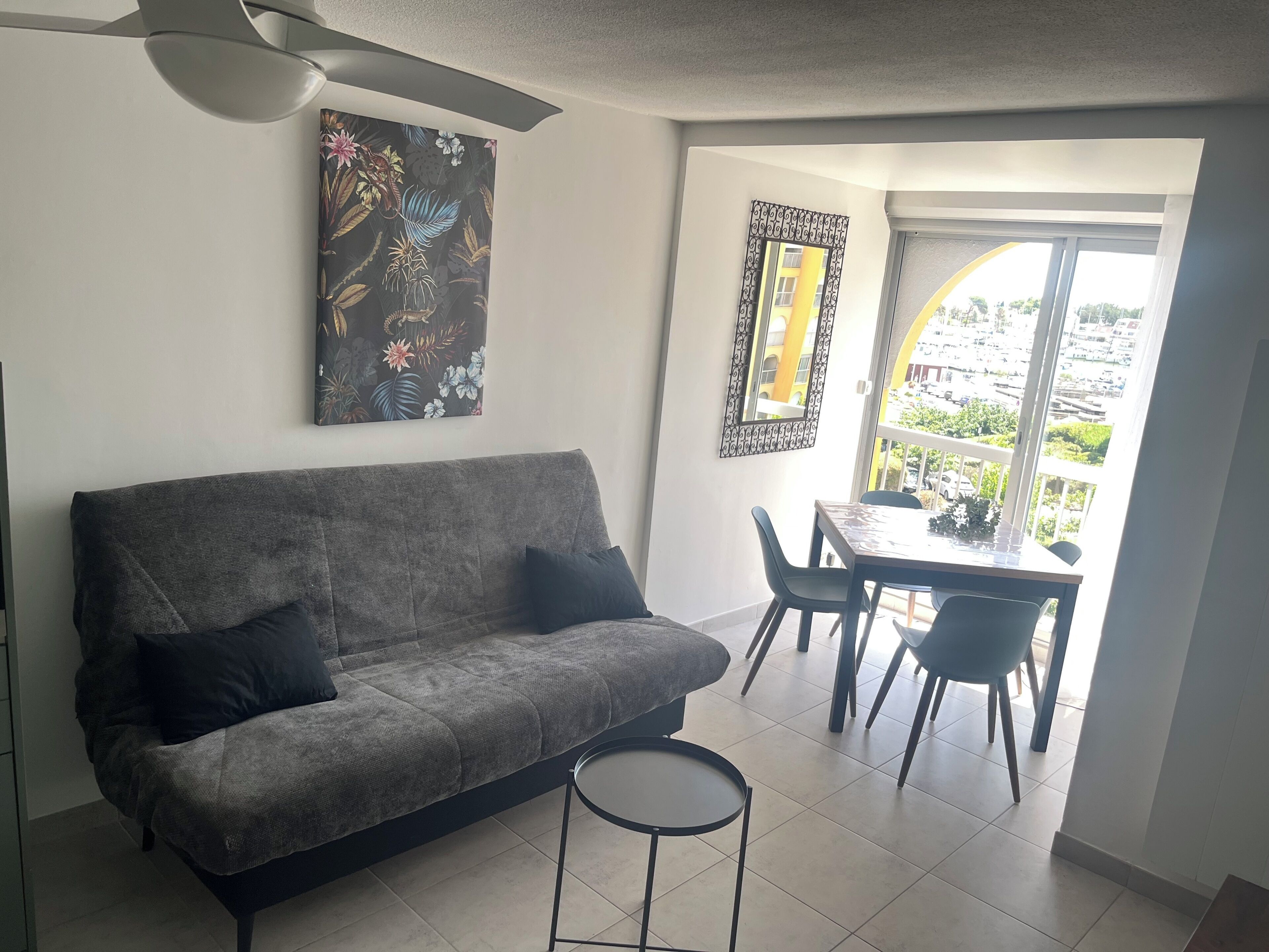 A living room with a grey sofa, a small round table, and a dining area with chairs.