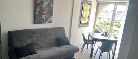 Una sala de estar con un sofá gris, una mesita redonda y un comedor con sillas.