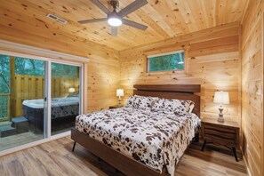 A wooden cabin bedroom with a bed, a nightstand, a window, and a ceiling fan.
