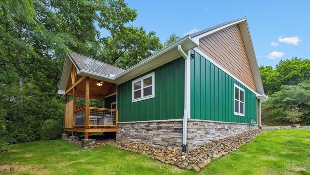 A two-story house with a stone foundation, green siding, and a wooden deck. - Dollys Cabins 1010  - Walk to Dollywood! (Pigeon Forge)