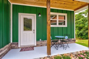 A green house with a white door, a window, and a porch with a table and chairs. - Dollys Cabin 1012  - Walk to Dollywood! (Pigeon Forge)
