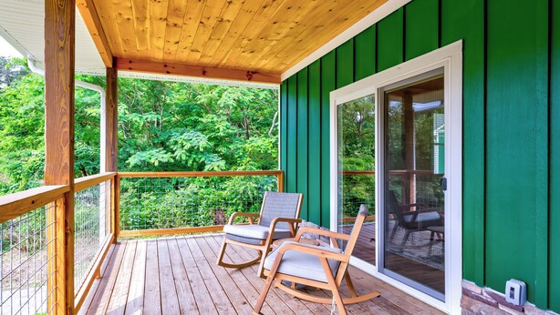 A wooden deck with two rocking chairs and a glass door leading to a green-painted room. - Dollys Cabin 1012  - Walk to Dollywood! (Pigeon Forge)
