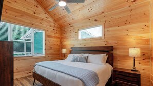 A wooden-paneled bedroom with a bed, two bedside lamps, and windows with blinds. - Dollys Cabin 1012  - Walk to Dollywood! (Pigeon Forge)