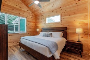 Ein Schlafzimmer mit Holzwänden, einem Bett, zwei Nachttischlampen und Fenstern mit Jalousien.