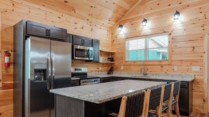 A modern kitchen with a stainless steel refrigerator, a built-in microwave, and a granite countertop. - Dollys Cabin 1012  - Walk to Dollywood! (Pigeon Forge)