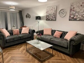 A living room with two dark grey sofas, a glass coffee table, and a floor lamp. - House Sleeps 6 With Enclosed Garden (Birkenhead)