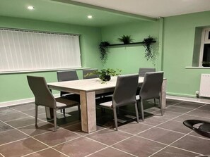 A dining area with a table and chairs, a window with blinds, and a radiator. - House Sleeps 6 With Enclosed Garden (Birkenhead)