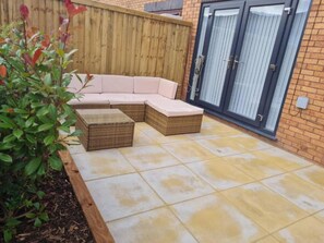 A patio with a sectional sofa and two ottomans, a wooden fence, and a glass door. - House Sleeps 6 With Enclosed Garden (Birkenhead)