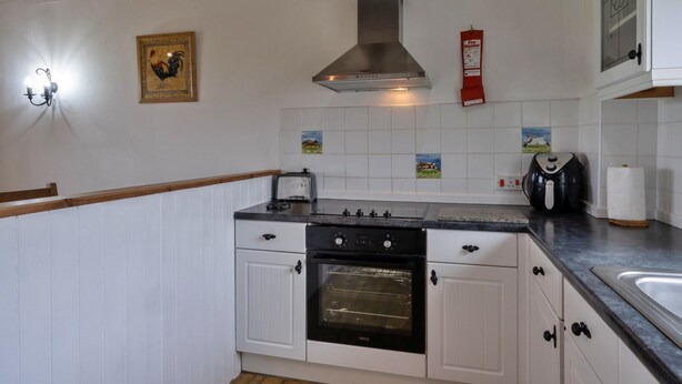 A kitchen with white cabinets, a stainless steel range hood, a toaster, and a fire blanket on the wall. - Scenic Snowdonia Border Cottage for 4 (Bude)