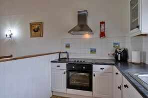 Cocina con armarios blancos, campana extractora de acero inoxidable, un tostador y una manta ignífuga en la pared.