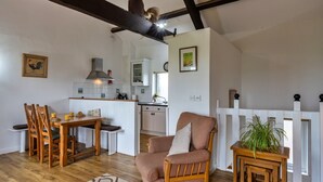 A cozy living room with a wooden dining table, a cushioned armchair, and a small side table with a plant. - Scenic Snowdonia Border Cottage for 4 (Bude)