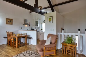 A cozy living room with a wooden dining table, a cushioned armchair, and a small side table with a plant. - Scenic Snowdonia Border Cottage for 4 (Bude)