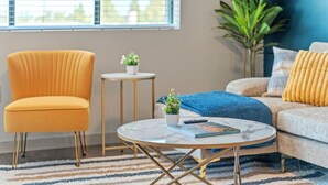 A living room with a yellow armchair, a round coffee table with a book and remote, a sofa with a blue throw, and a plant. - 2BR Desert Getaway - Pool, King Beds, Hot Tub, Gym (Tempe)