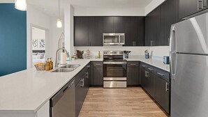 A modern kitchen with dark cabinetry, stainless steel appliances, and a white countertop. - 2BR Desert Getaway - Pool, King Beds, Hot Tub, Gym (Tempe)