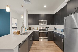 A modern kitchen with dark cabinetry, stainless steel appliances, and a white countertop. - 2BR Desert Getaway - Pool, King Beds, Hot Tub, Gym (Tempe)