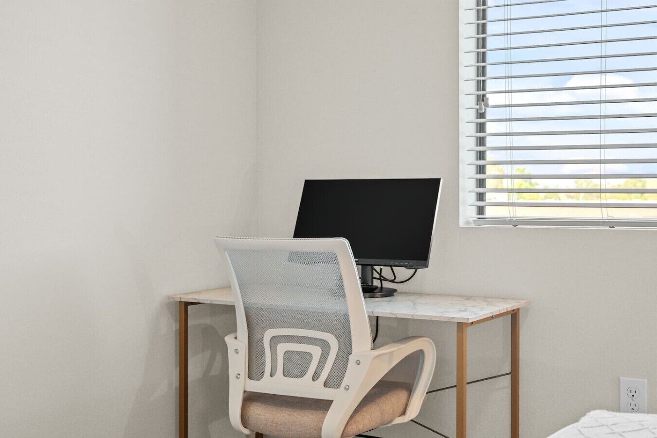 A workspace with a computer on a desk, a chair, and a window with blinds.
