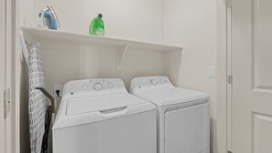 A laundry room with two white washing machines, a drying rack, and a shelf with a blue iron and a green bottle. - 2BR Desert Getaway - Pool, King Beds, Hot Tub, Gym (Tempe)