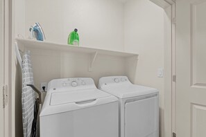 A laundry room with two white washing machines, a drying rack, and a shelf with a blue iron and a green bottle. - 2BR Desert Getaway - Pool, King Beds, Hot Tub, Gym (Tempe)