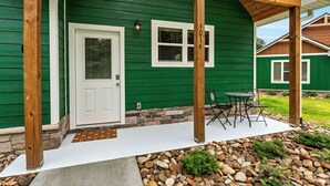 A green house with a covered porch, a white door, and a stone foundation. - Dollys Cabins 1014 - Walk to Dollywood! (Pigeon)
