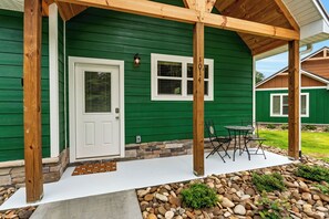 A green house with a covered porch, a white door, and a stone foundation. - Dollys Cabins 1014 - Walk to Dollywood! (Pigeon)