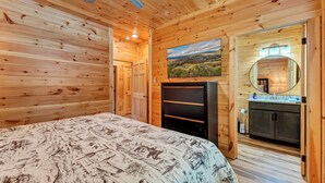 A wooden room with a bed, a dresser, a mirror, and a painting on the wall. - Dollys Cabins 1014 - Walk to Dollywood! (Pigeon)